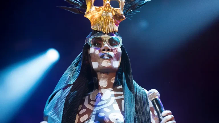 Grace Jones wearing a helmet adorned with a golden skull and retro glasses during a stage performance in 2018, photographed by Bruce Baker in Sydney, Australia.