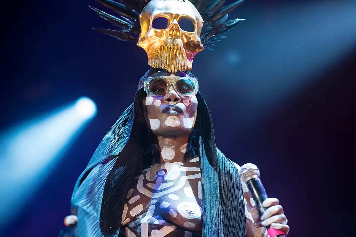 Grace Jones con un casco adornado con una calavera dorada y gafas retro durante una actuación en 2018, fotografiada por Bruce Baker en Sídney, Australia.