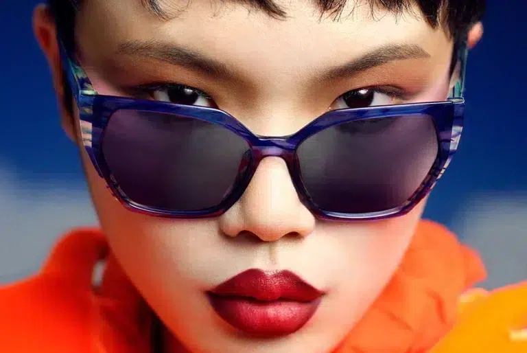 Retrato de una mujer con gafas de sol modernas de la colección SS25 de Etnia Barcelona, con montura azul translúcida.