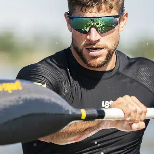 Atleta de kayak llevando gafas deportivas Rudy Project Turbolence, remando con intensidad en el agua.