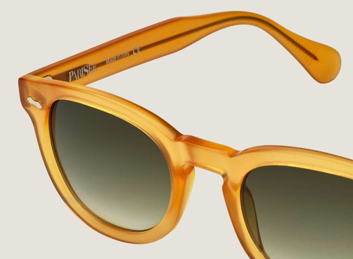 Detalle de gafas de sol Dorata, primer plano de la montura en acetato amarillo miel transparente, remache en rombo, lentes verdes degradadas, marcado PARISEE Made in Italy en la patilla