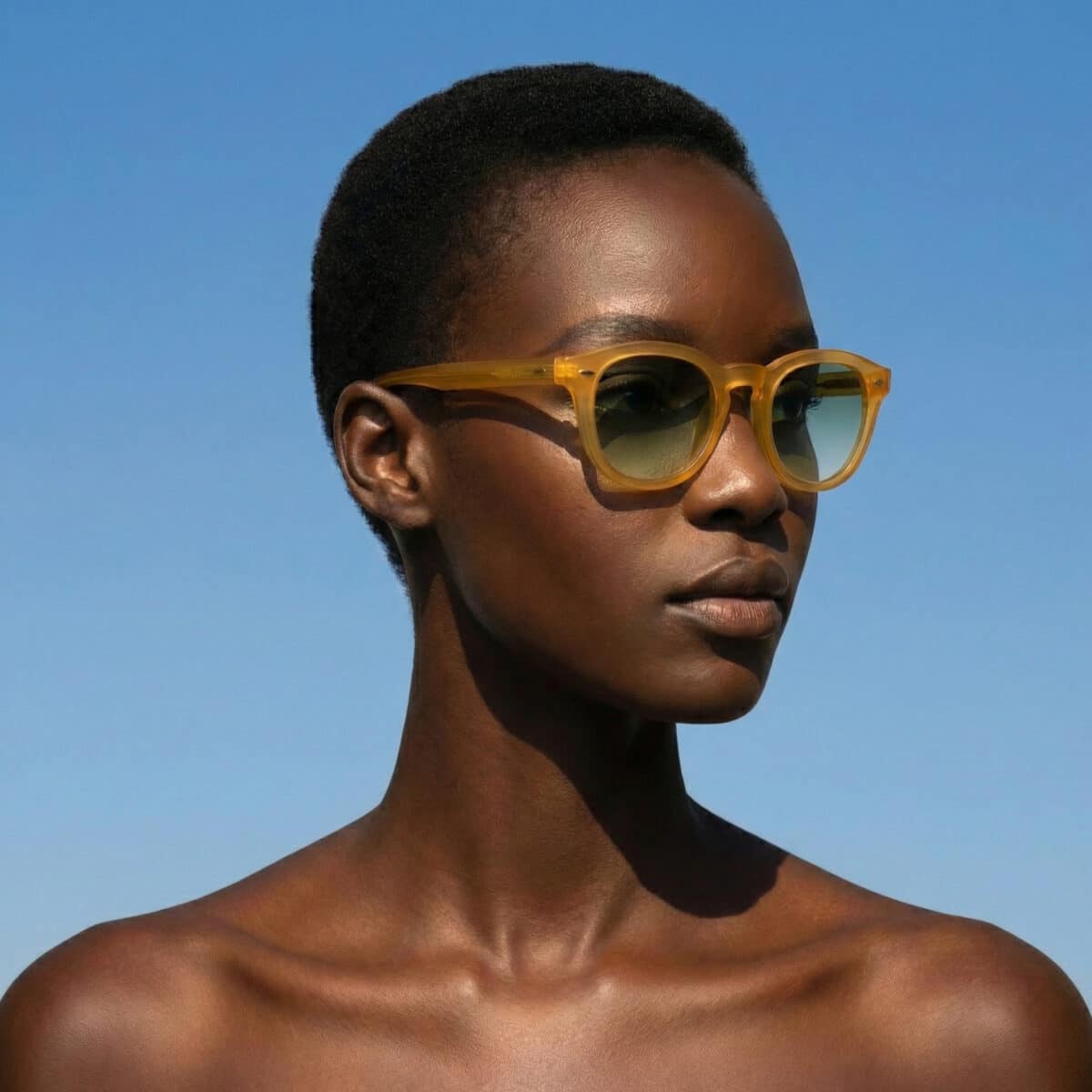 Retrato en exterior de una modelo con gafas de sol Dorata en acetato amarillo miel transparente y lentes verdes degradadas, cielo azul de fondo