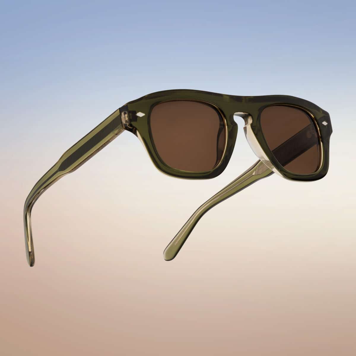 Vista trasera en tres cuartos de las gafas de sol Freschezza en acetato verde oliva translúcido con lentes marrones, sobre fondo de cielo degradado