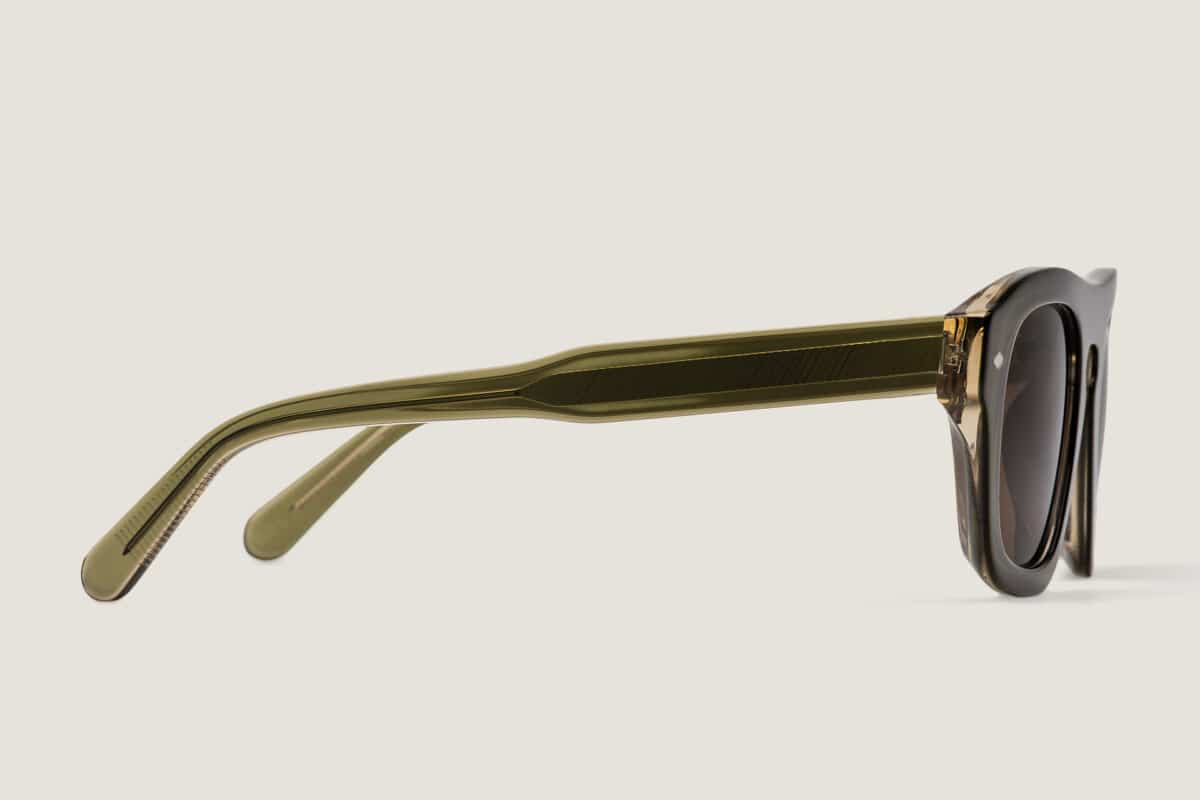 Vista de perfil de las gafas de sol Freschezza en acetato verde oliva translúcido con lentes marrones, sobre fondo beige claro