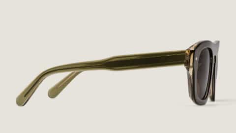 Vista de perfil de las gafas de sol Freschezza en acetato verde oliva translúcido con lentes marrones, sobre fondo beige claro