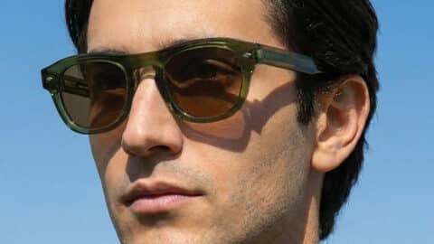 Retrato al aire libre de un hombre con las gafas de sol Freschezza en acetato verde oliva translúcido con lentes marrones, con cielo azul de fondo