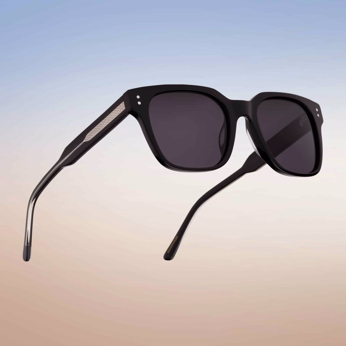 Lunettes de soleil Essentiel N1 en acétate noir polie avec verres gris foncé, vue de profil ouverte sur fond dégradé ciel
