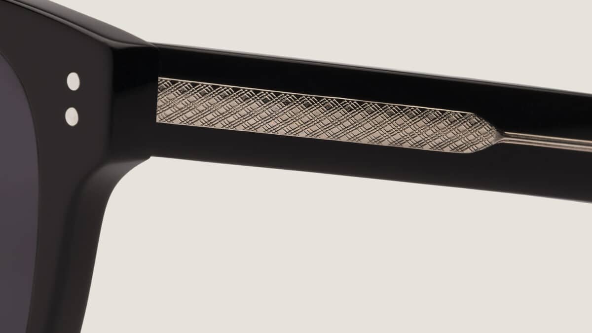 Primer plano de la varilla de las gafas de sol Essentiel N1 en acetato negro mate con inserto metálico grabado y doble remache
