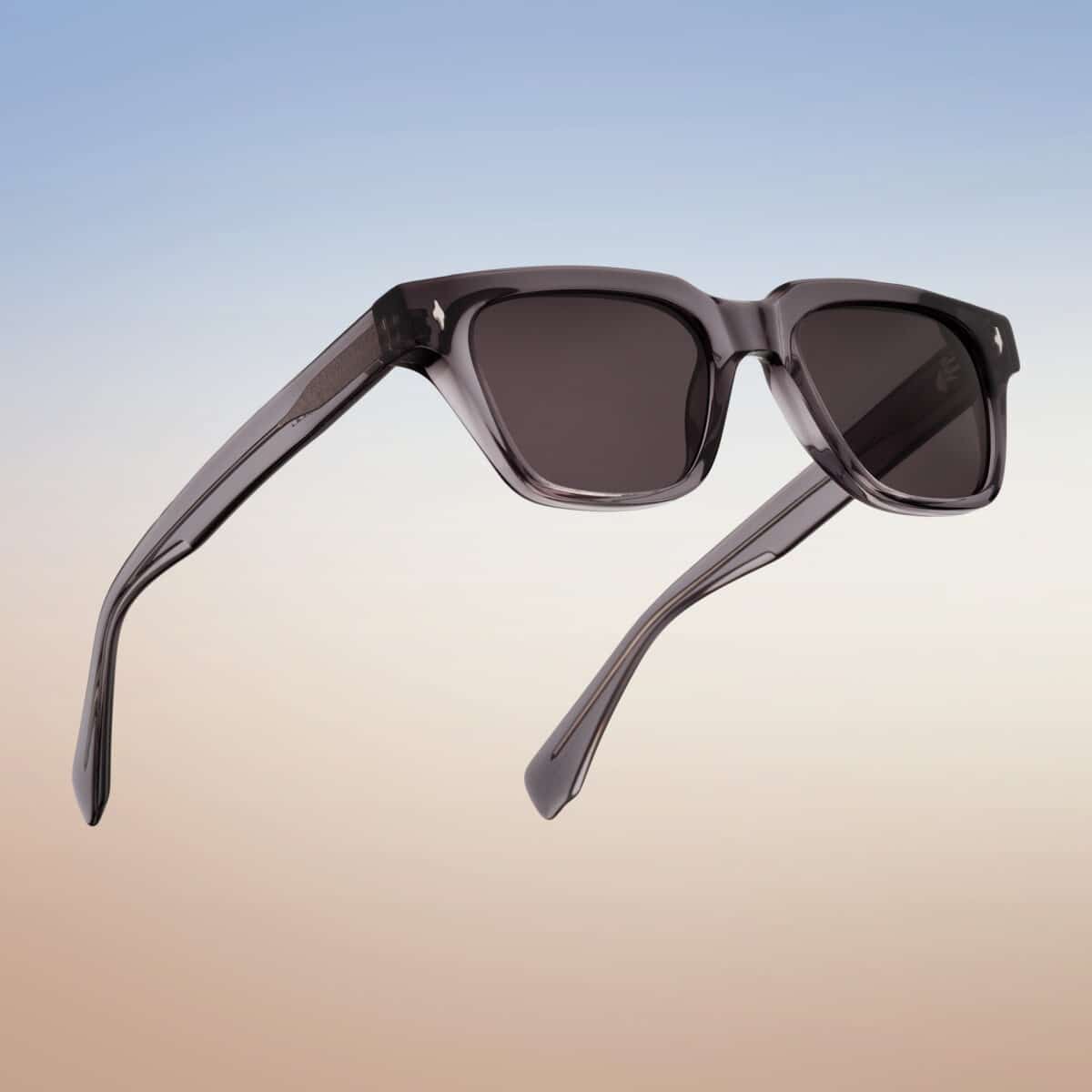 Vista “en uso” de las gafas de sol Essentiel N2 sobre un degradado de cielo: montura rectangular de acetato ahumado translúcido con lentes gris oscuro