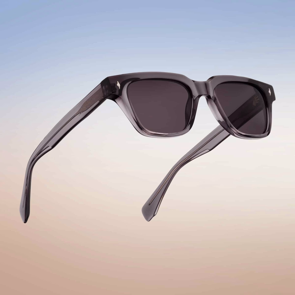 Vista “en uso” de las gafas de sol Essentiel N2 sobre un degradado de cielo: montura rectangular de acetato ahumado translúcido con lentes gris oscuro